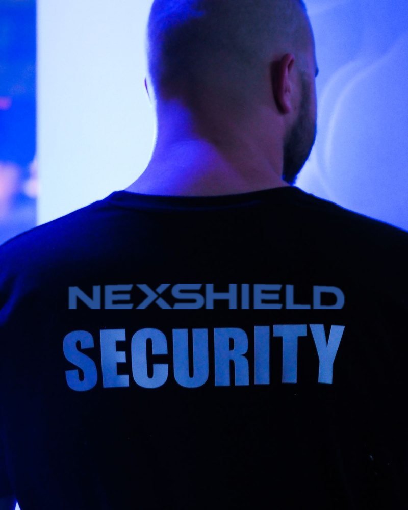 NEXSHIELD SECURITY officer on duty, photographed from behind with the company name across the back of the uniform