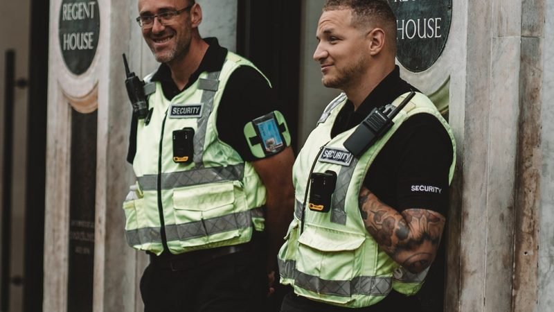 Two licensed security officers in hi-vis vests on static guard duty at a building entrance